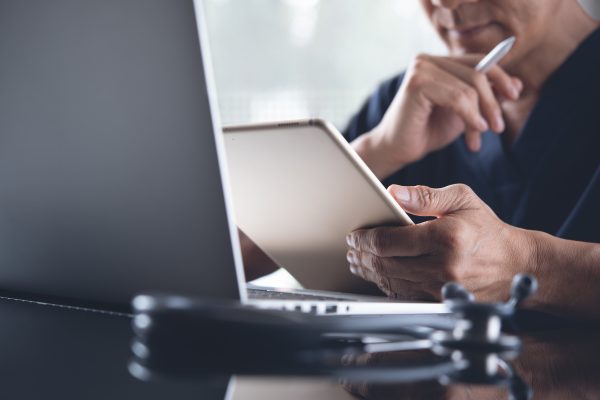 Close up of male doctor, medical student or surgeon using digital tablet while working on laptop computer during the video conference